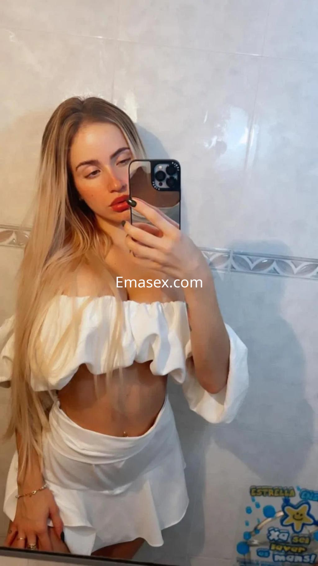 La puta en Vigo lleva un conjunto blanco de dos piezas con mangas amplias, mostrando su abdomen y cabello rubio.