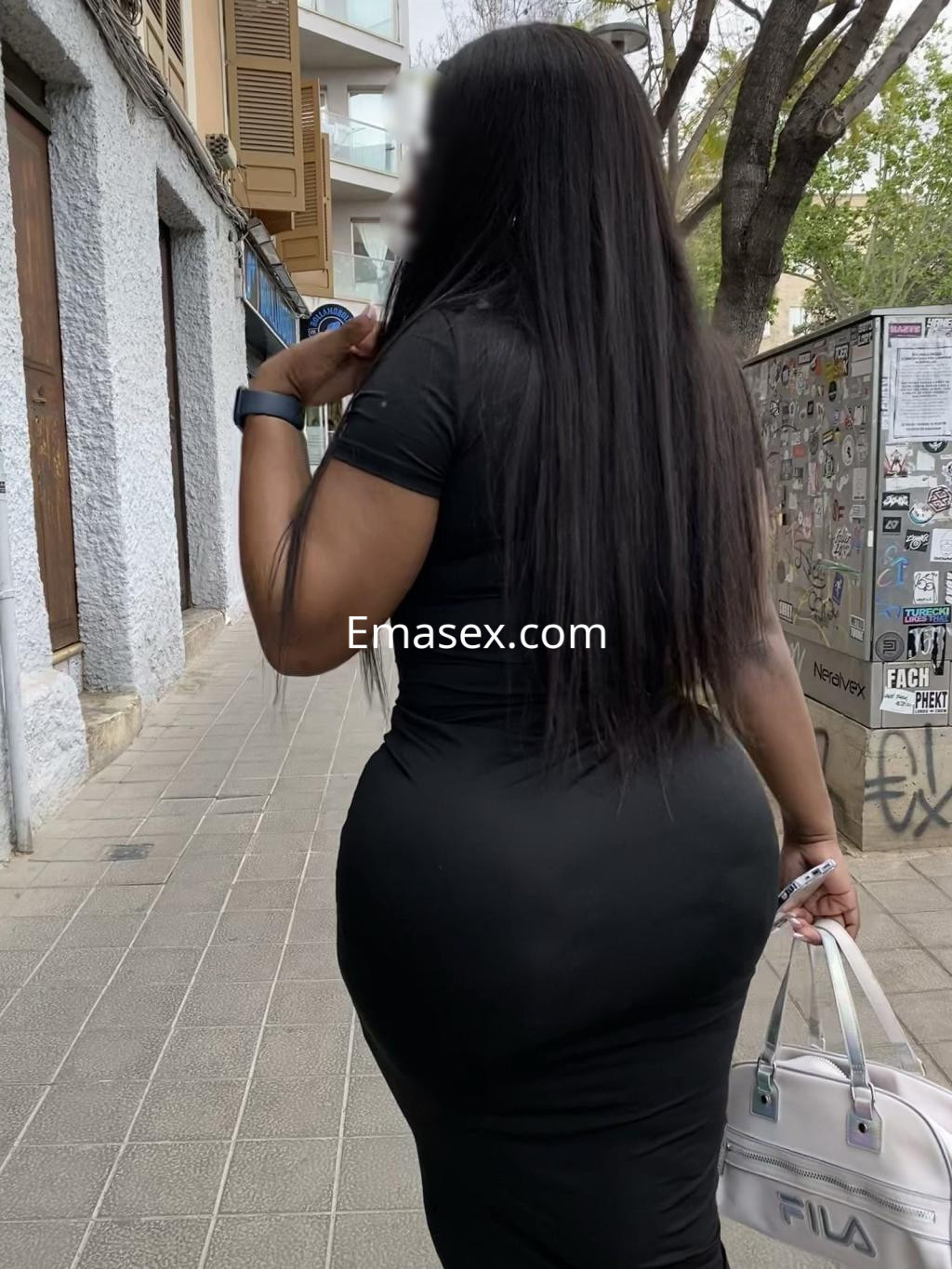 Escort de Palma de Mallorca con vestido negro ajustado y cabello largo, caminando por una calle urbana.