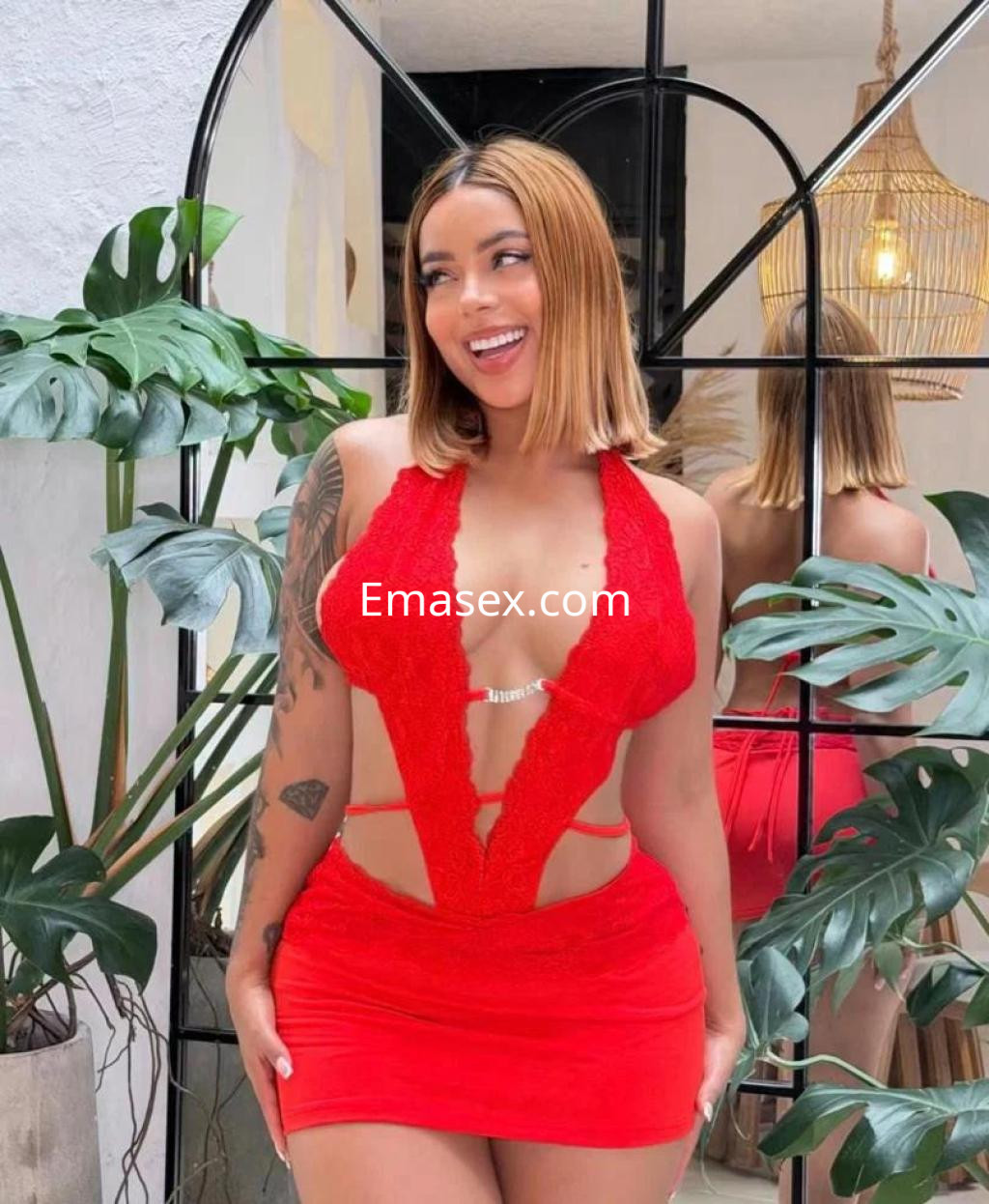 Escort en Murcia con cabello rubio y vestido rojo ajustado, posando sonriente frente a un espejo.