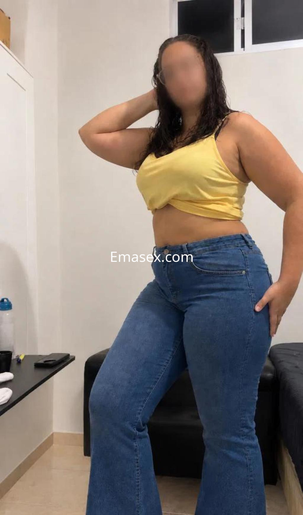 Puta posando en una habitación con top amarillo y jeans ajustados, mostrando su figura en Murcia.