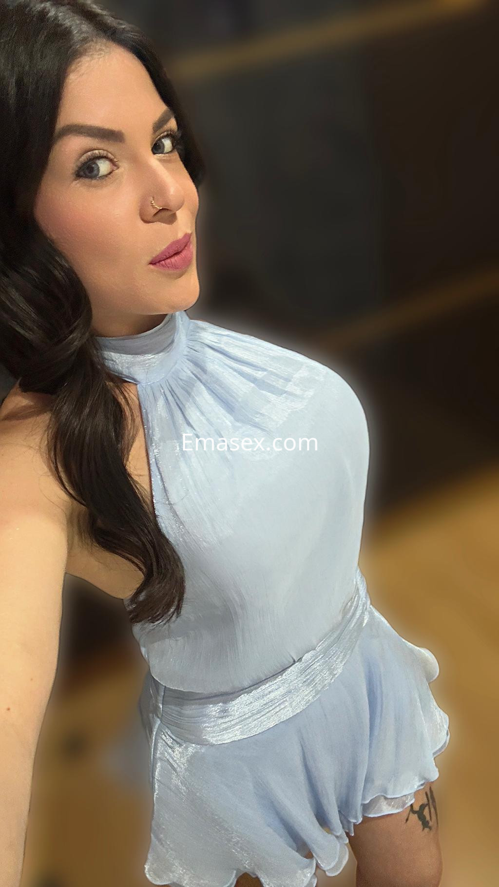 Escort en Santiago con cabello oscuro y rizado, vistiendo un conjunto de color azul claro y luciendo un maquillaje destacado.