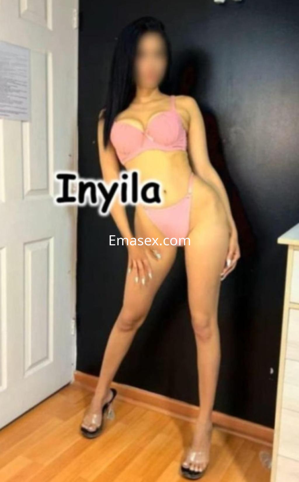 Puta en Madrid vestida con bikini rosa claro, posando de pie con una pierna adelante en un fondo oscuro.