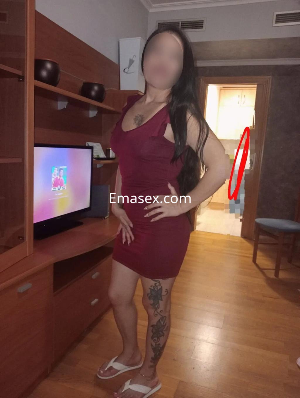 Puta en Albacete, con cabello largo y oscuro, vistiendo un vestido rojo ajustado y sandalias, posando en una habitación.