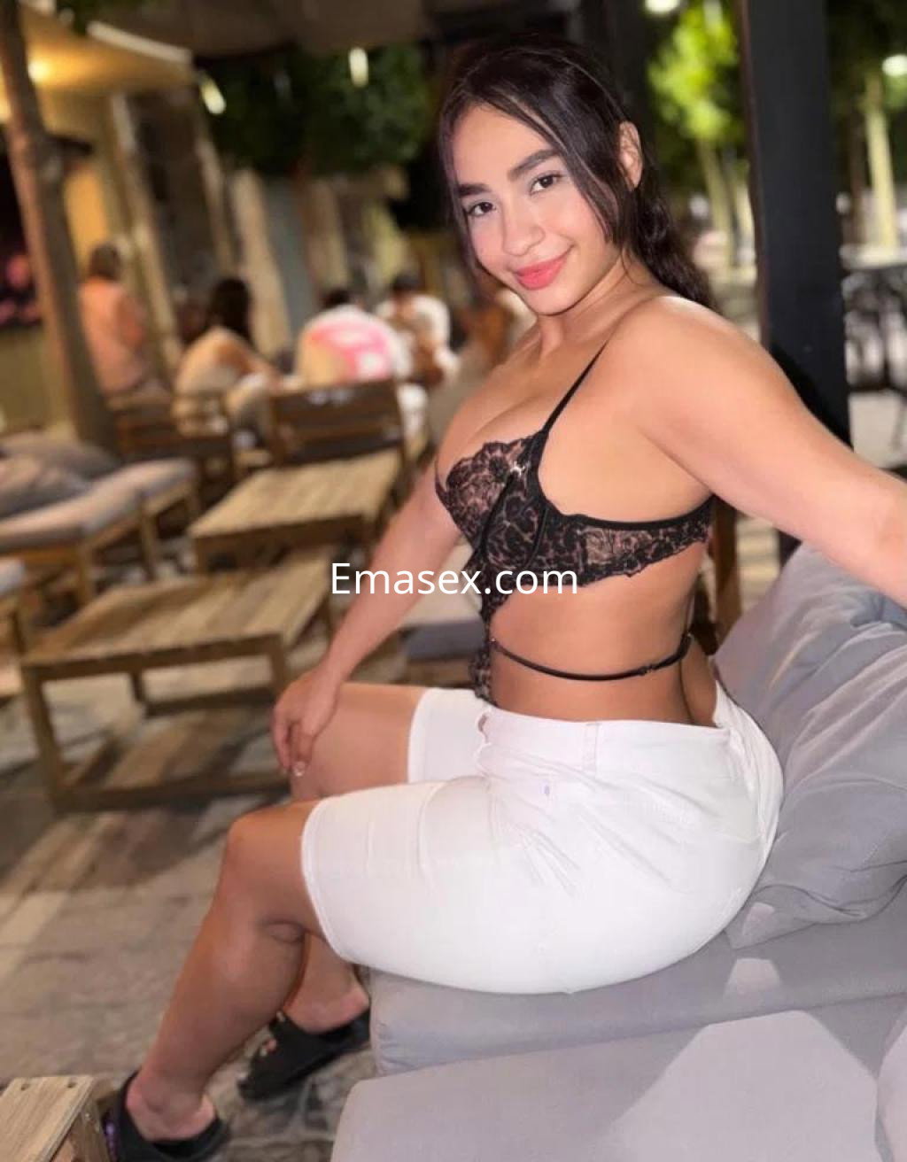 La puta luce un top de encaje negro y pantalones cortos blancos, sentada en un sofá en Almería.