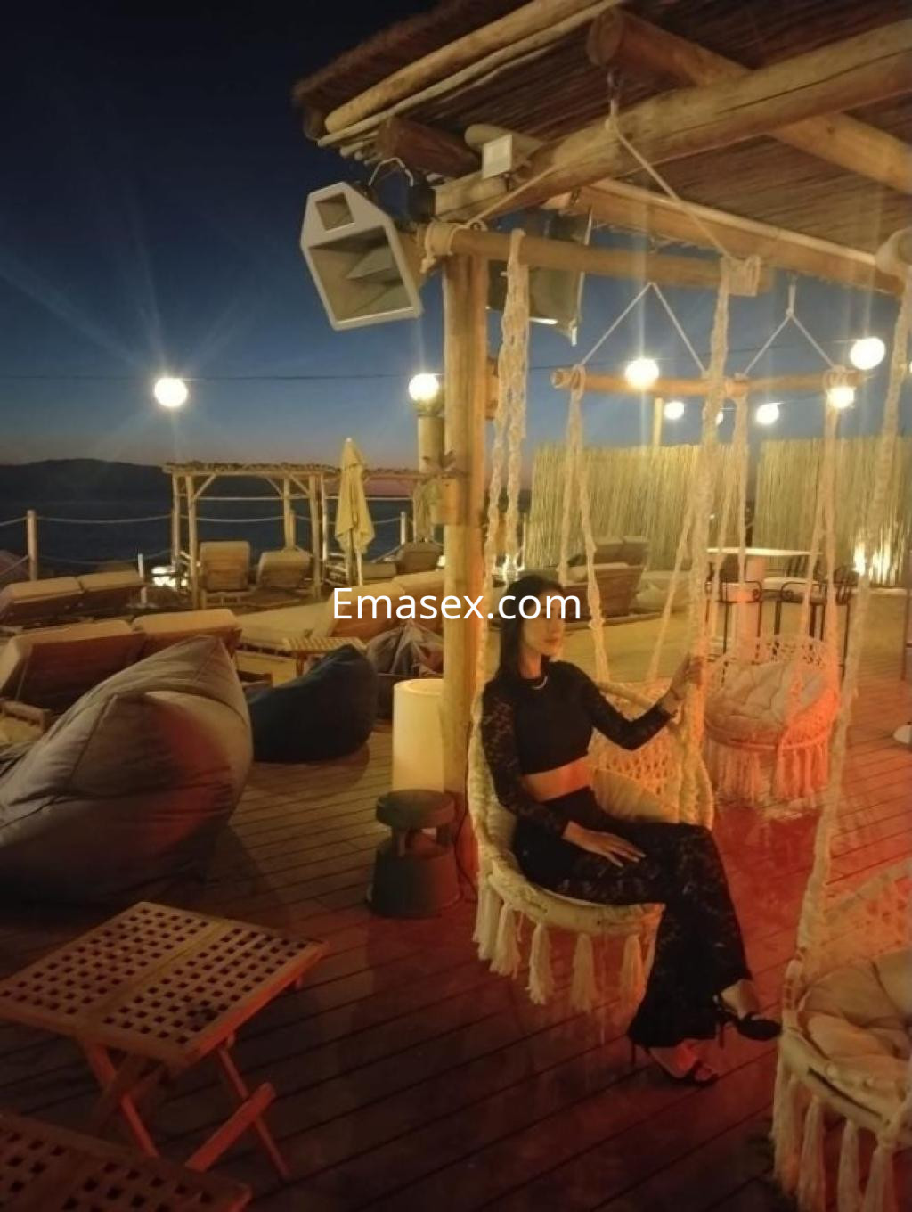 Escort sentada en una hamaca de un ambiente acogedor en Tenerife, vestida con un conjunto negro y tacones.