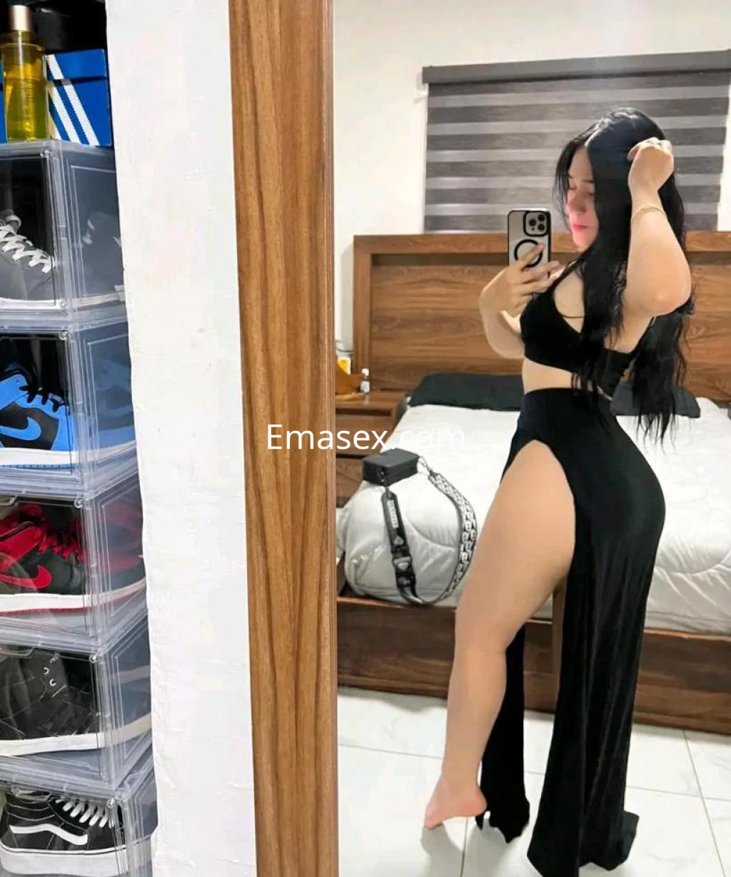 Escort en Tenerife, posando frente a un espejo con un conjunto negro que destaca su figura y una pierna al descubierto.