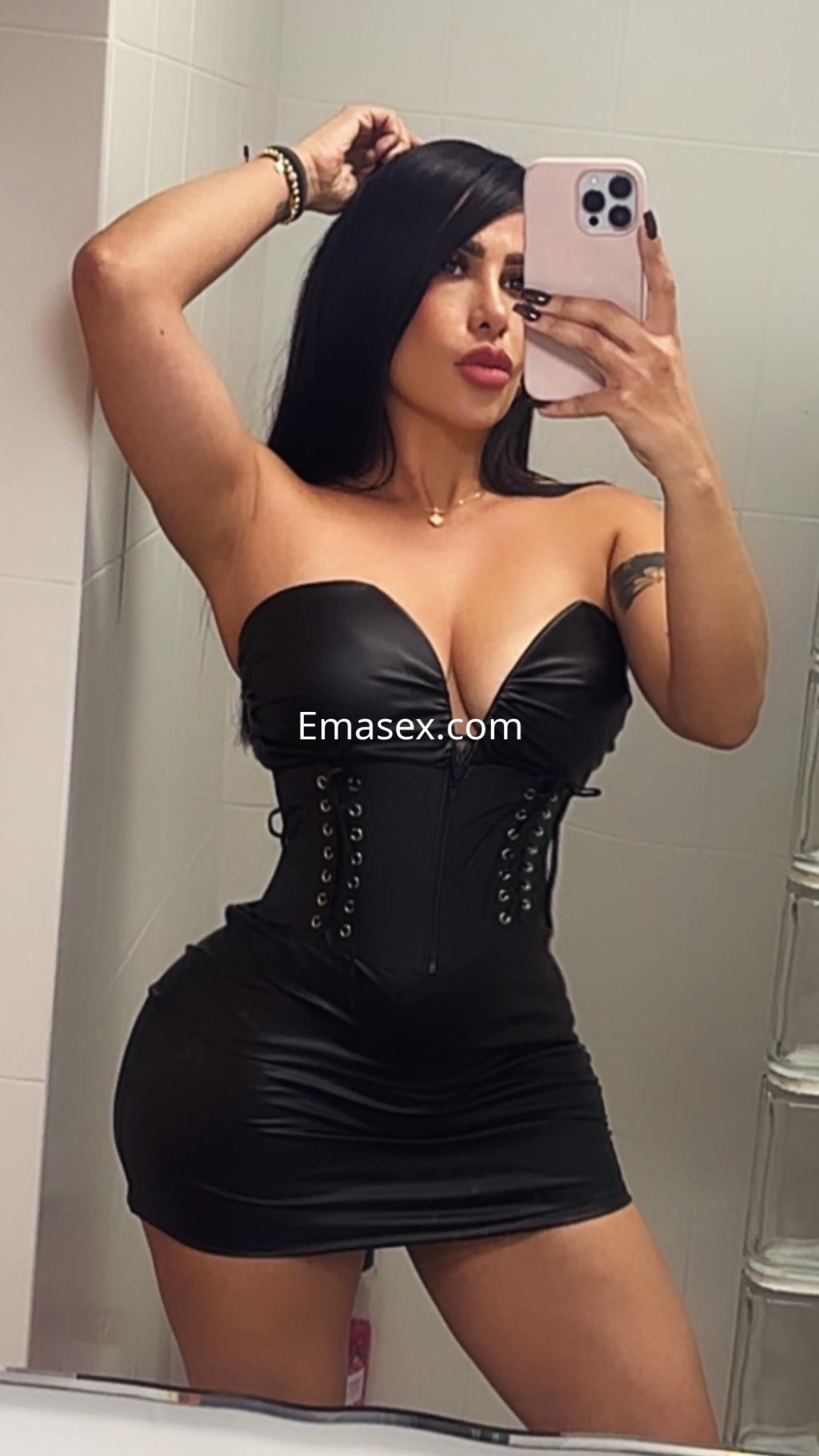 Puta en Murcia con un vestido negro ajustado y tirantes, posando frente a un espejo en un baño.