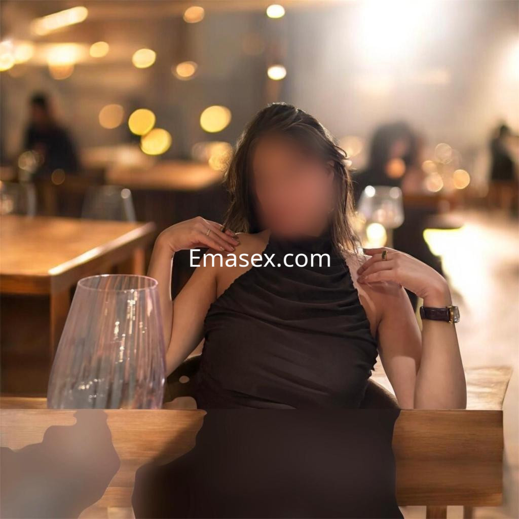 Escort en Zaragoza con vestido negro ajustado, posando en un ambiente elegante y desenfocado de un restaurante.