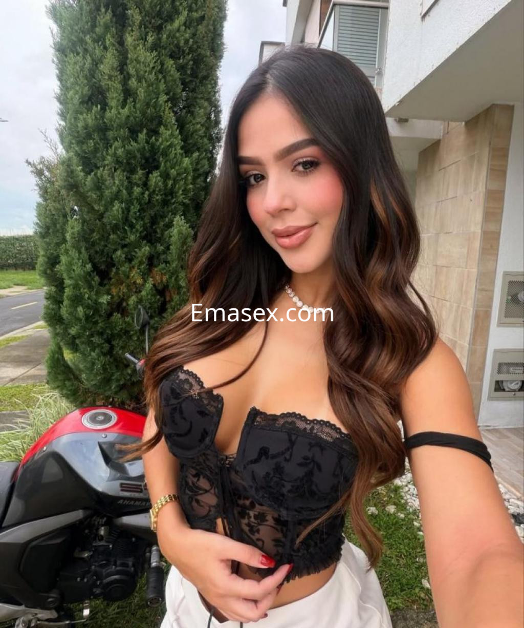 Escort en Girona posando frente a una moto, vistiendo un corset negro con detalles y una falda clara.