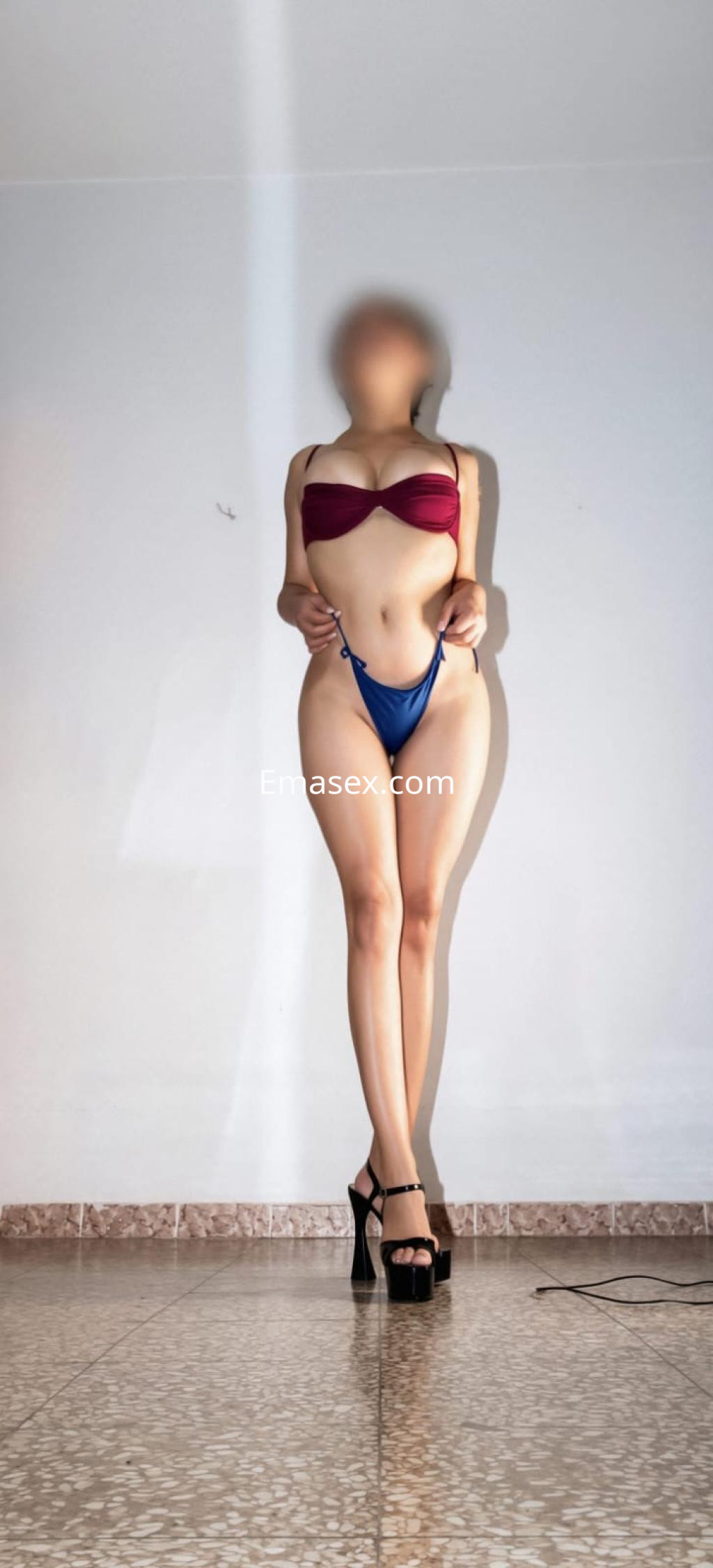 Escort en Madrid con top bicolor rojo y azul, usando una lencería ajustada y tacones altos en un ambiente neutro.
