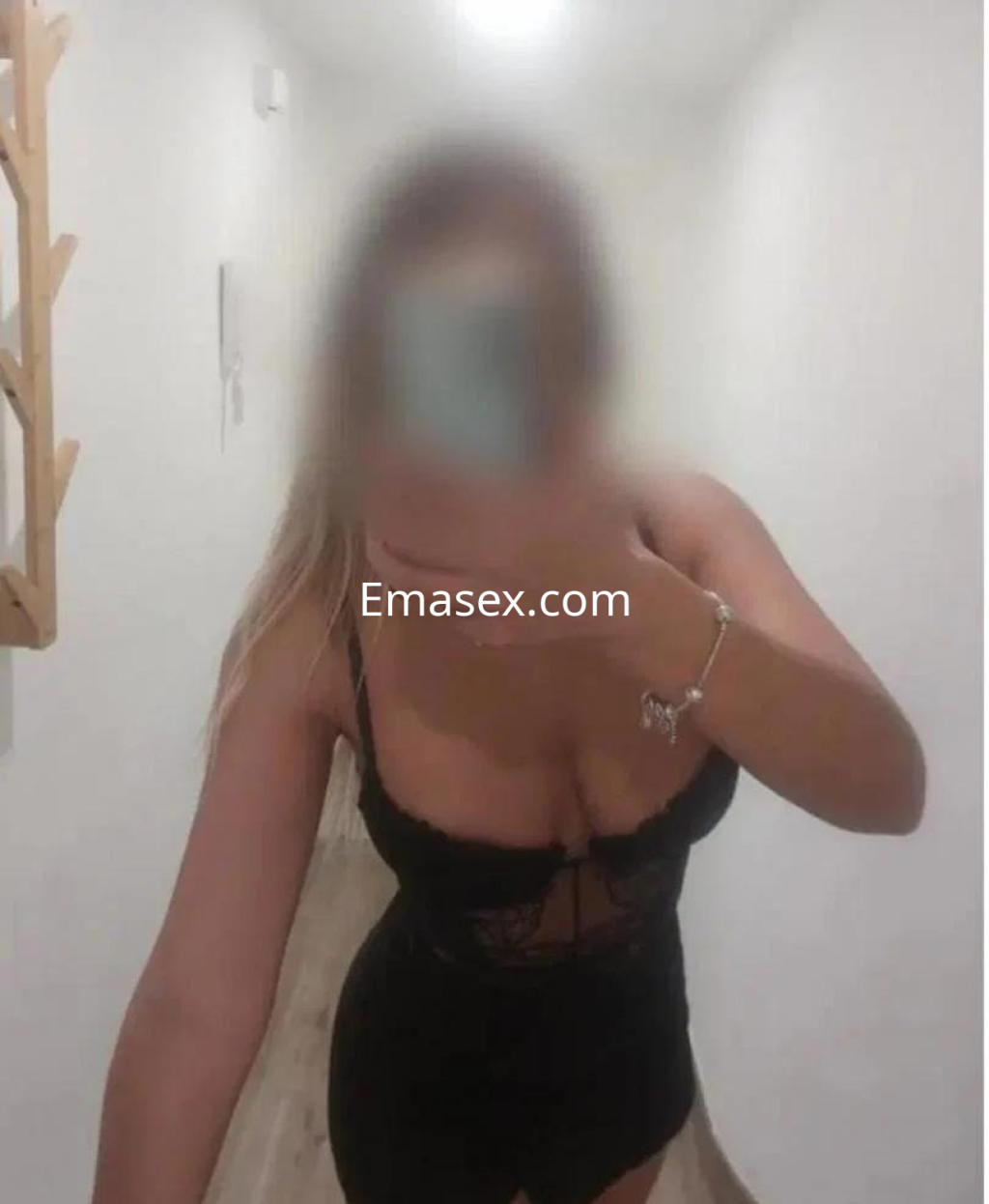 Escort en Burgos luciendo un body negro con detalles de encaje, en un pasillo iluminado y de paredes blancas.