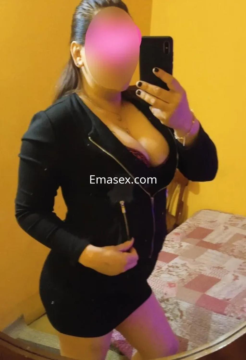 Escort en Gijón, posando frente a un espejo con un vestido negro ajustado y una chaqueta, mostrando una figura esbelta.
