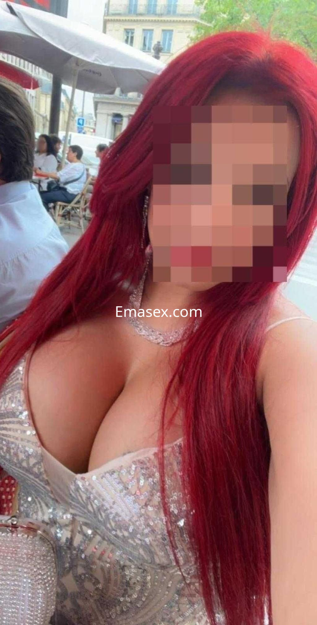 Puta en Madrid con cabello largo y rojo, vistiendo un vestido brillante que destaca su escote en un ambiente al aire libre.