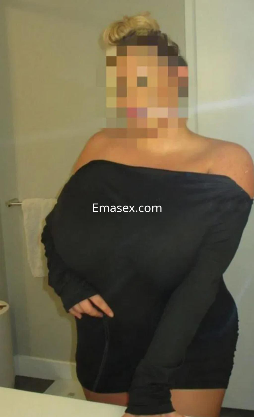 Puta en Logroño posando frente a un espejo, vistiendo un vestido negro ajustado y con el cabello recogido.