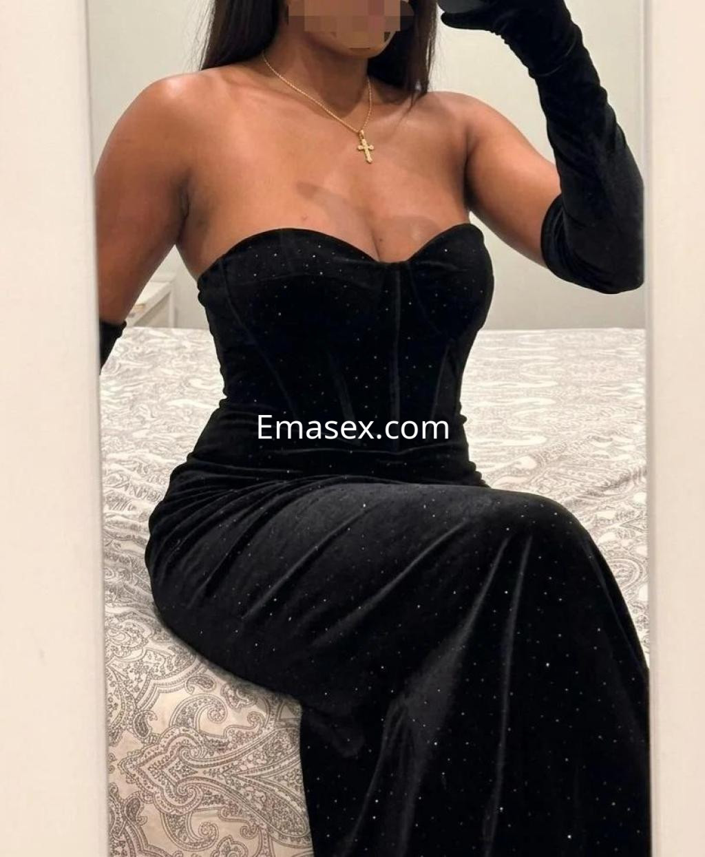 Escort sentada en una cama, luciendo un vestido negro ajustado y guantes largos, en un ambiente elegante de Madrid.