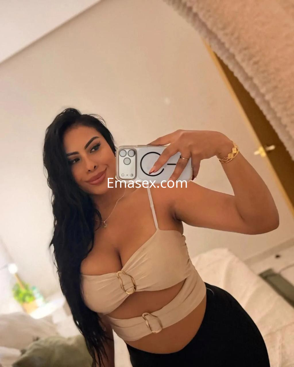 Escort en Palma de Mallorca, posando con un top claro y pantalones oscuros en un entorno acogedor.