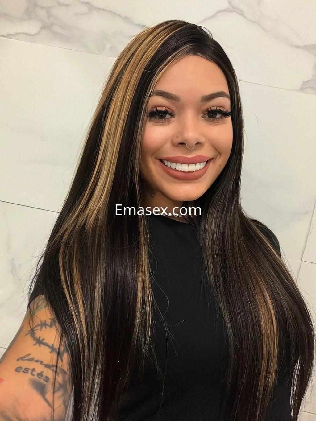 Escort en Palma de Mallorca con cabello largo y lacio, sonrisa amplia y top negro, posando frente a un fondo claro.