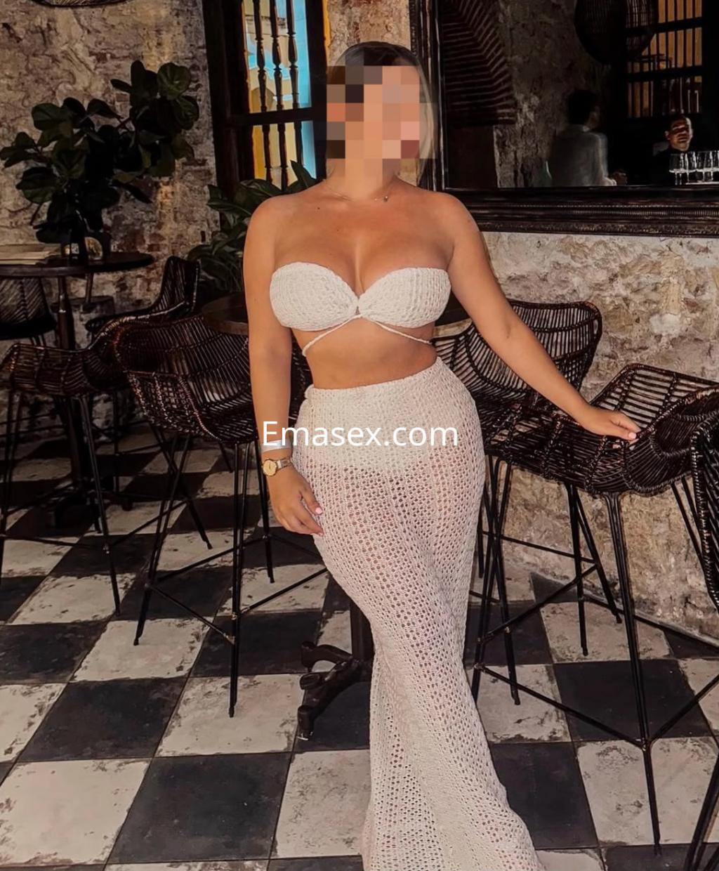 Puta en un bar de León, posando de pie con un vestido blanco de red que realza su figura.