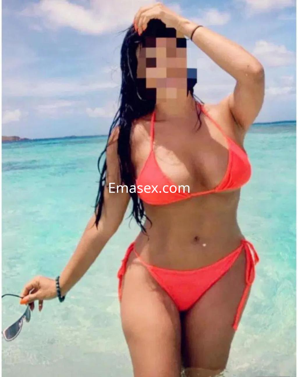 Puta en la playa de Toledo, luciendo un bikini naranja y posando con una mano en el cabello, frente al mar.