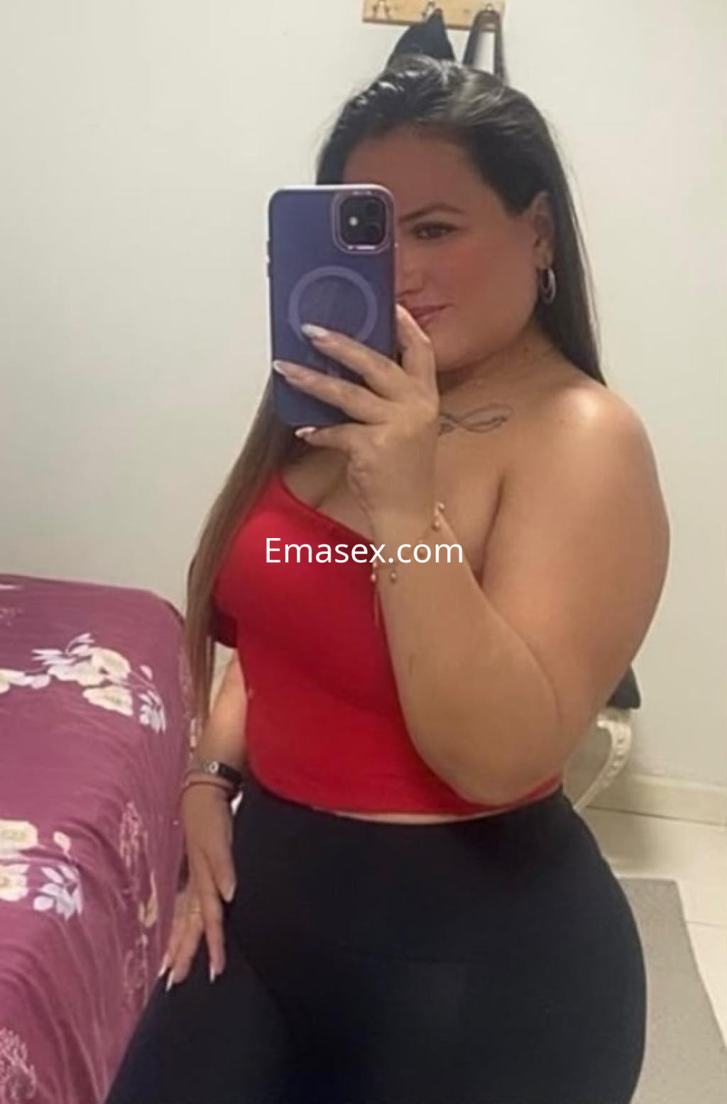 La puta en Santander se muestra con un top rojo y pantalones ajustados, sonriendo mientras se toma una selfie.