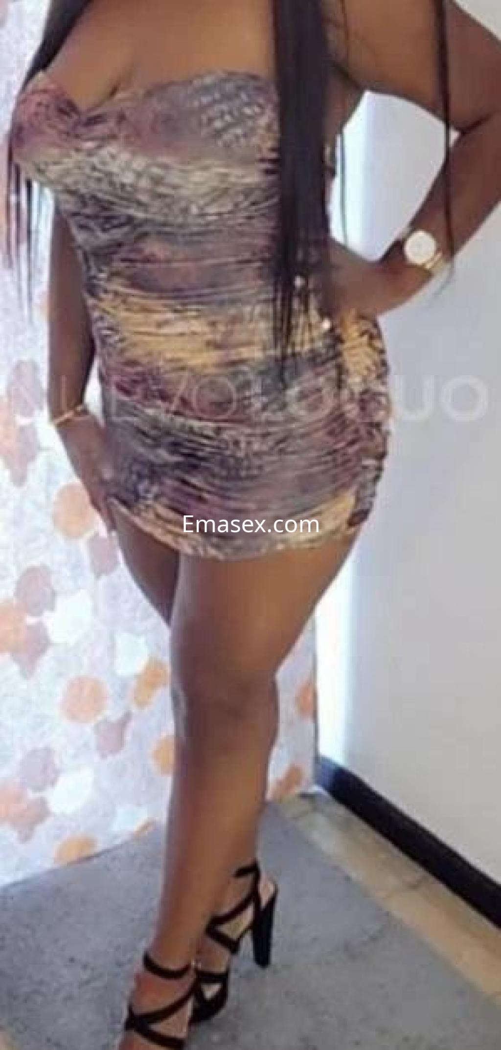 Escort en Toledo con vestido ajustado de colores vibrantes y tacones altos, posando con una mano en la cadera.