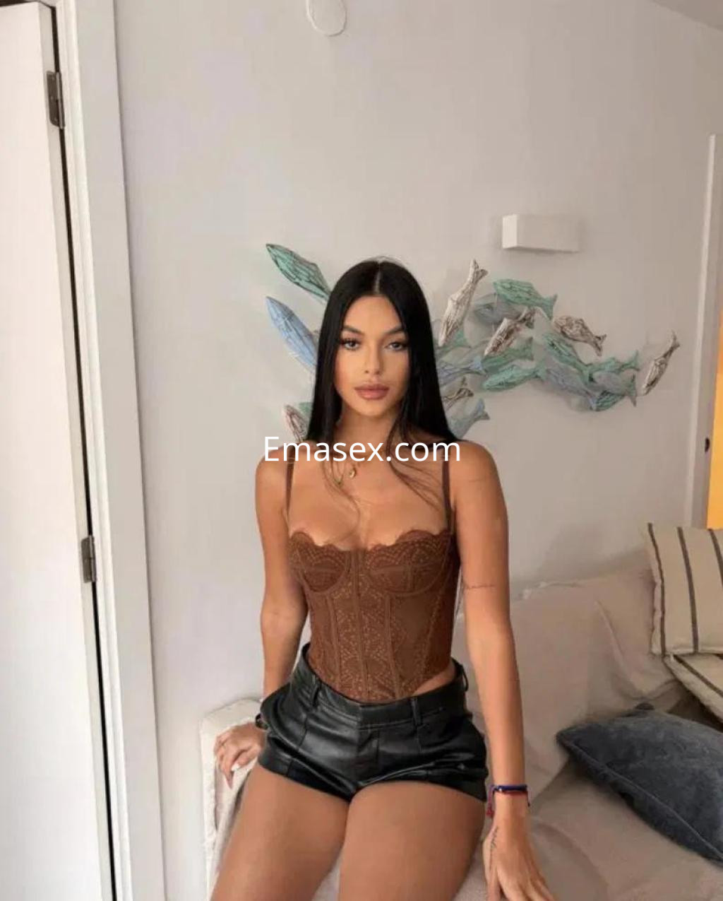 Escort en Badajoz con cabello largo y lacio, luciendo un corset marrón y shorts negros en un ambiente moderno.