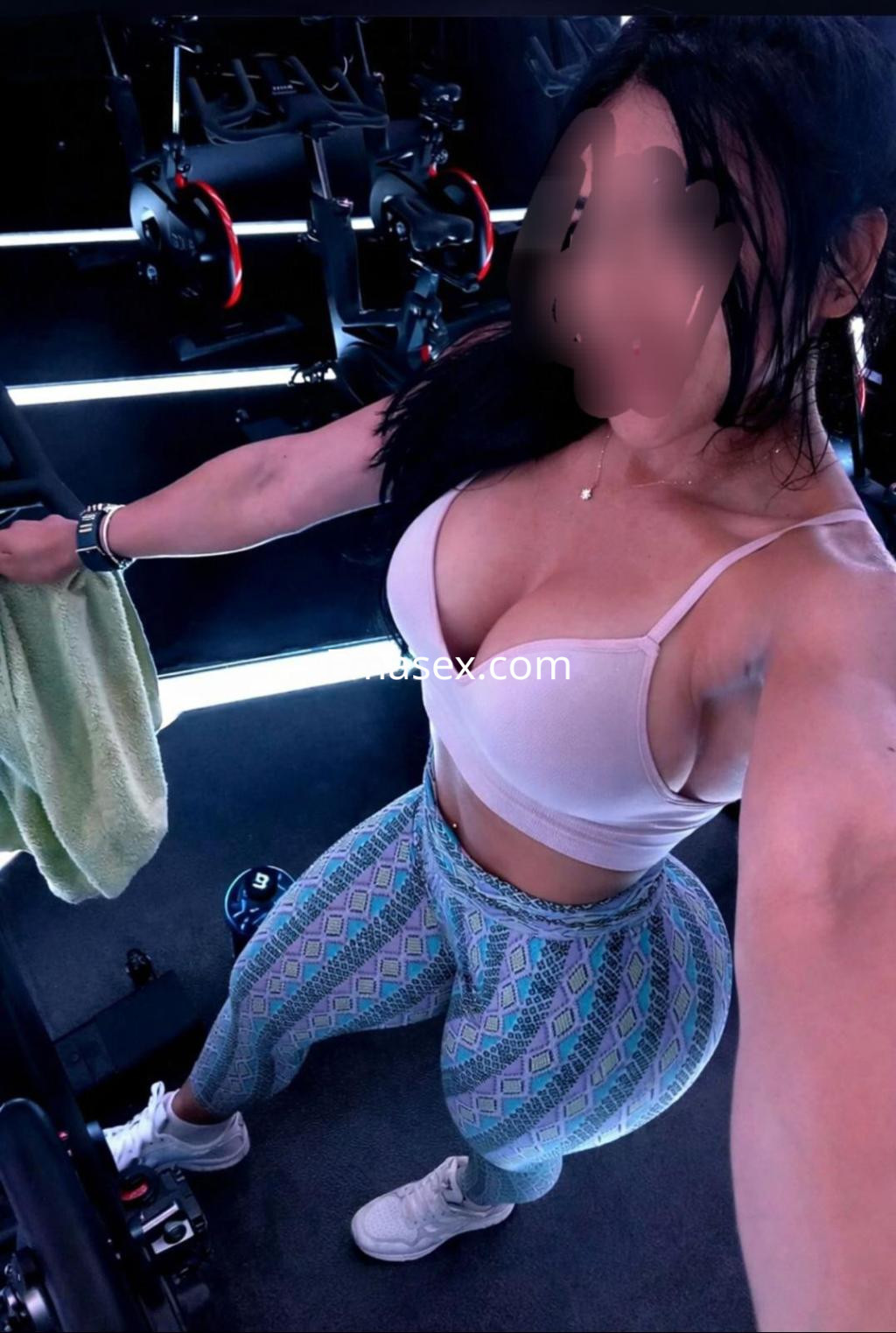 Escort en Oviedo, con cabello largo y oscuro, vistiendo un sujetador claro y leggings estampados en un gimnasio.