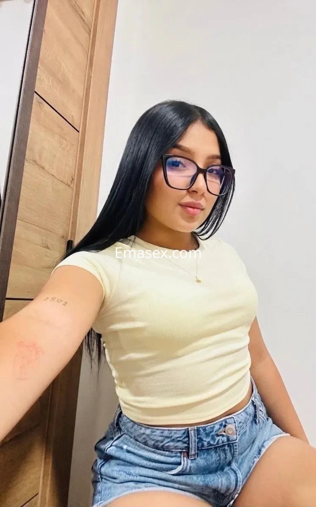 Escort en Vigo con cabello largo y lacio, usa una camiseta amarilla y shorts de mezclilla, posando sonriente.
