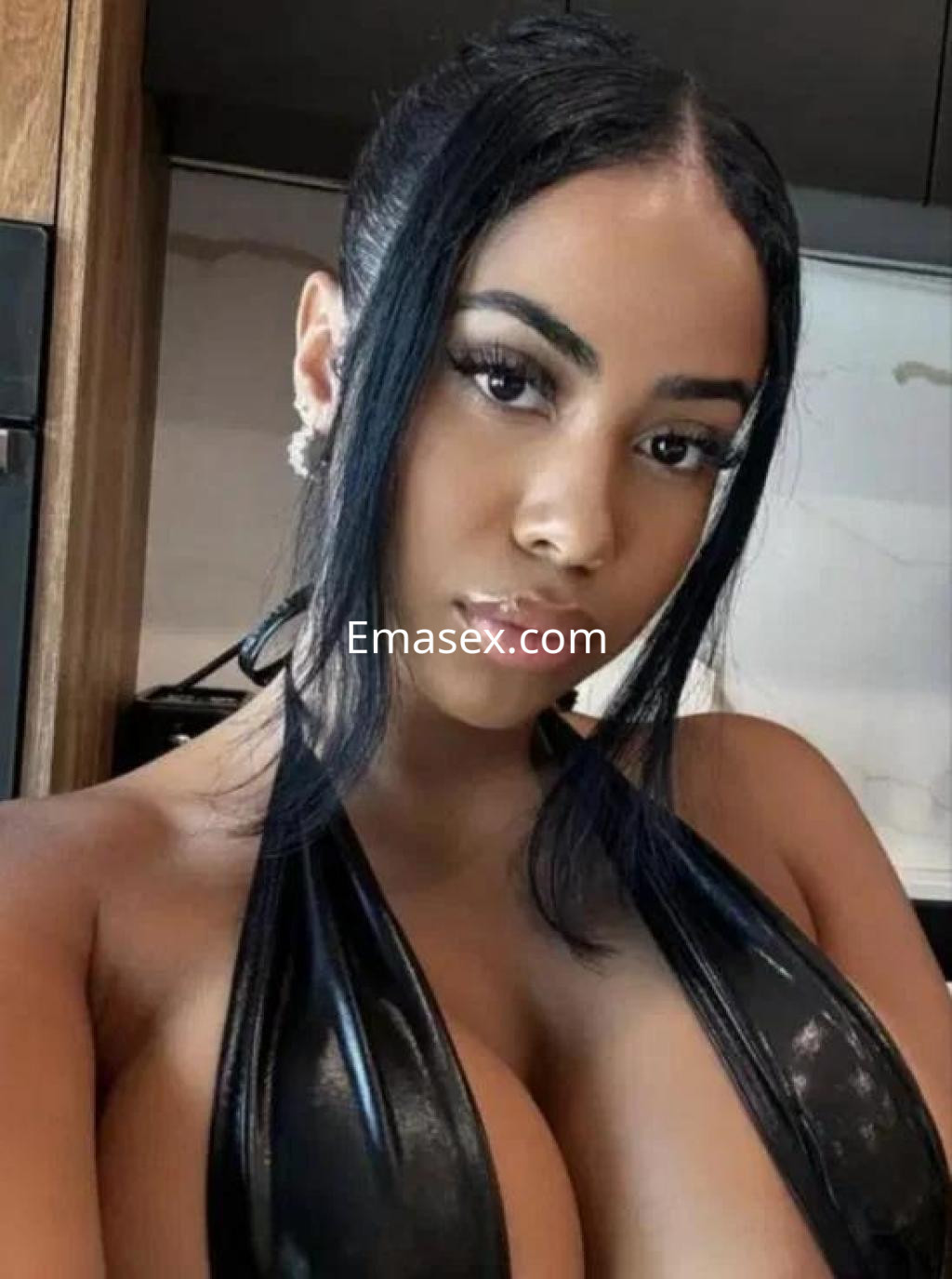 Puta con cabello oscuro y lacio, viste un top negro ajustado que resalta su figura en una cocina moderna de Badajoz.