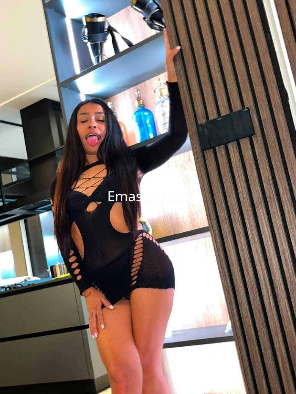 Escort en Tenerife luciendo un body negro con cortes, posando de manera sugestiva en un ambiente moderno.