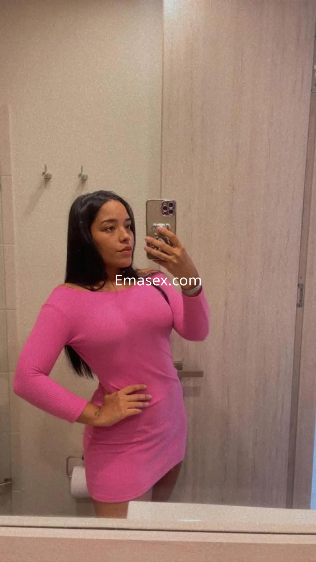 Escort en Valladolid con cabello largo y lacio, viste un vestido rosa ajustado y posa frente a un espejo.