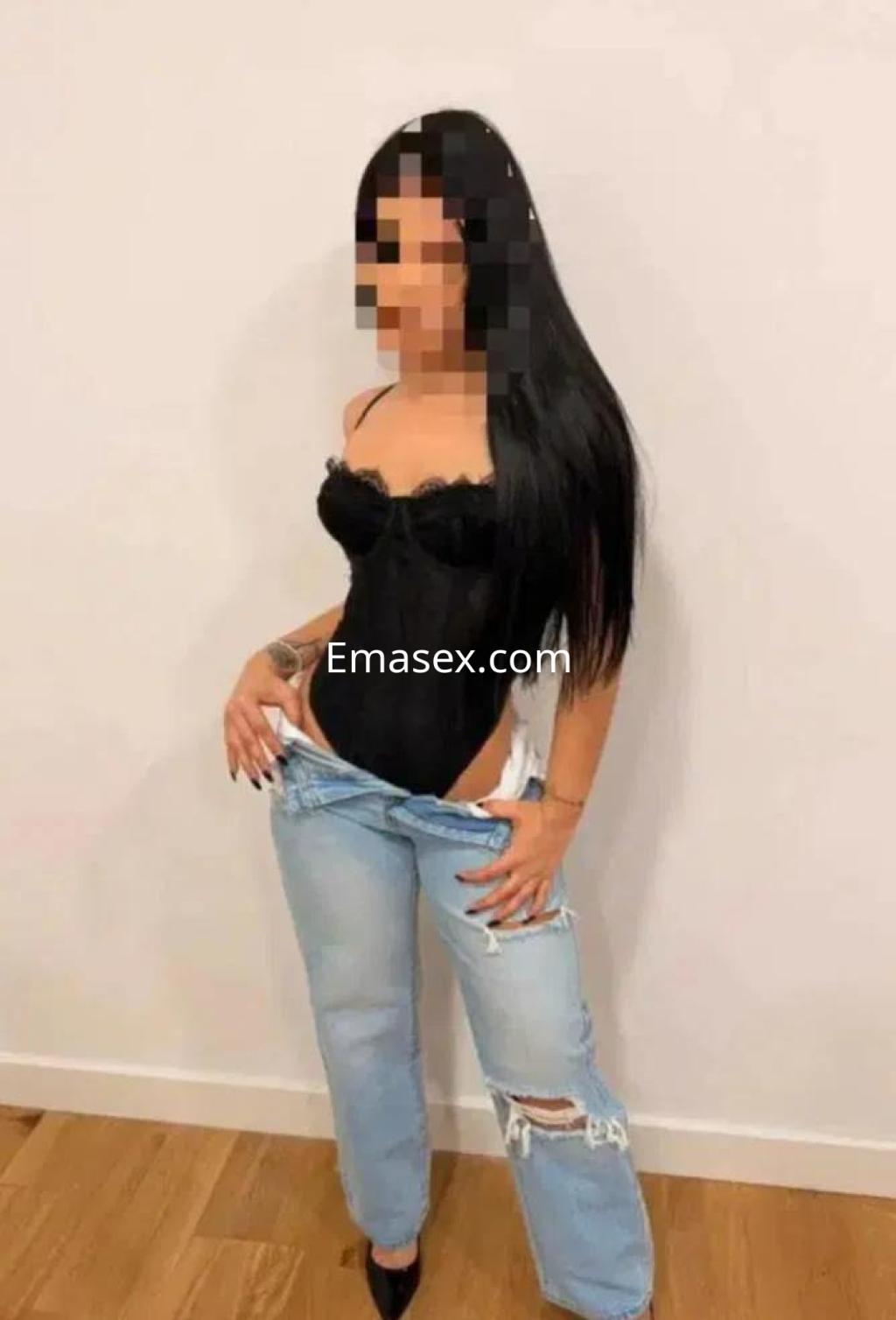 Escort en Burgos con cabello largo y oscuro, vistiendo corset negro y jeans desgastados, posando en un ambiente interior.