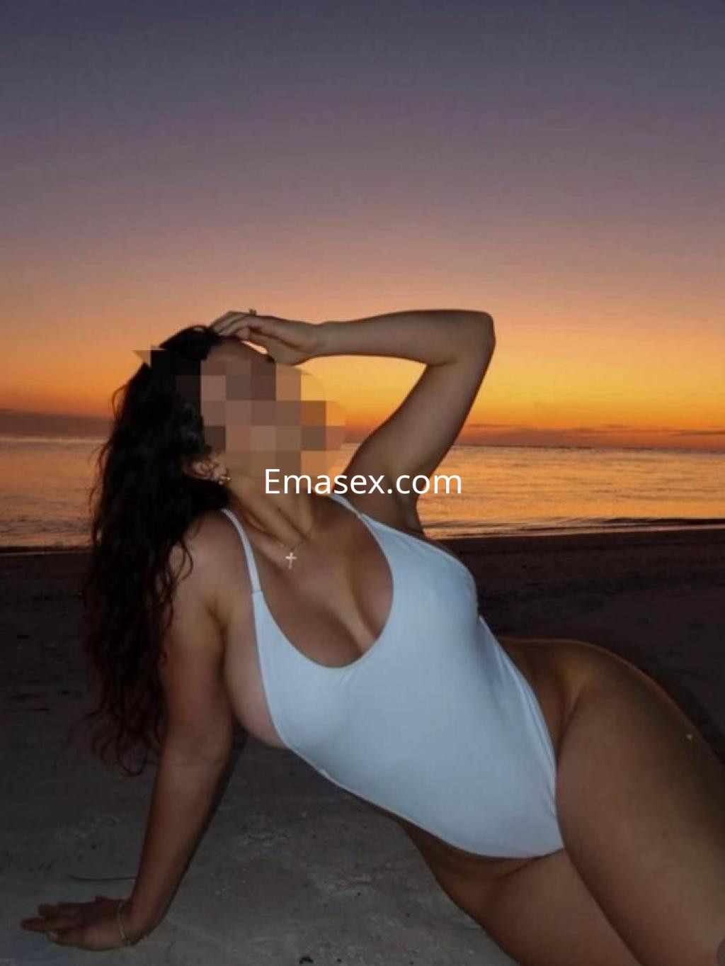 Puta en Vitoria posando en la playa al atardecer, luciendo un traje de baño blanco y con el cabello rizado.