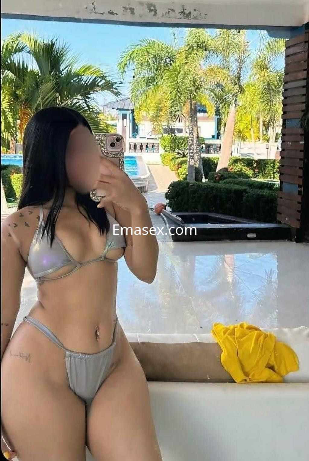 Puta en Pamplona luciendo un bikini plateado mientras se toma una selfie en un entorno de piscina.