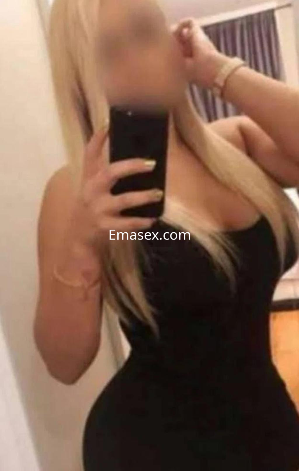 Escort en Almería con cabello largo y rubio, vistiendo un vestido negro ajustado mientras se toma una selfie.