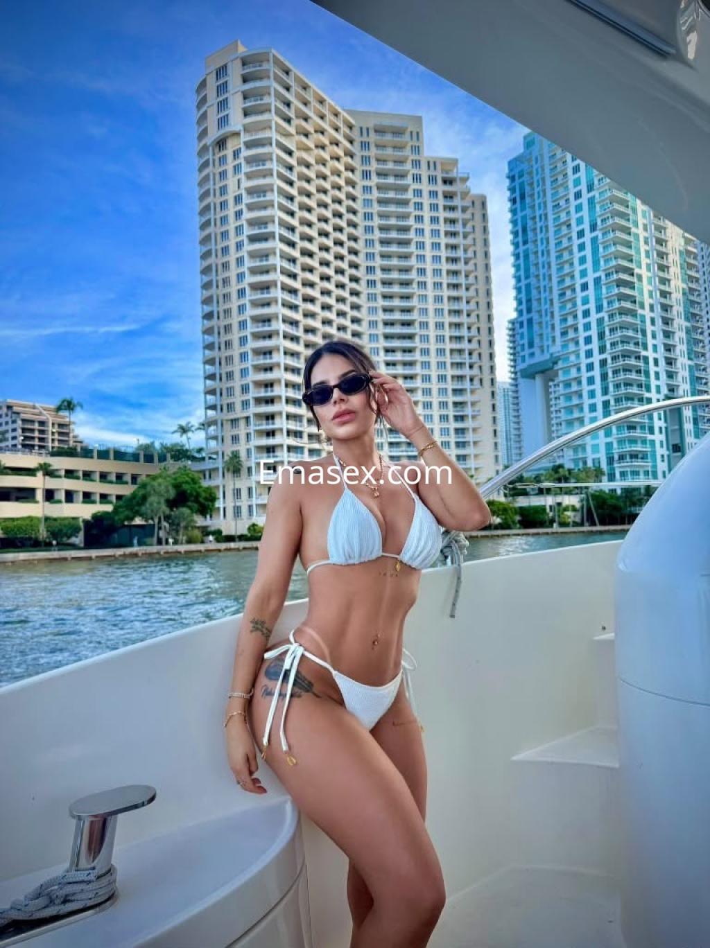 La puta luce un bikini blanco y gafas de sol, posando en un yate con rascacielos de fondo en Bilbao.