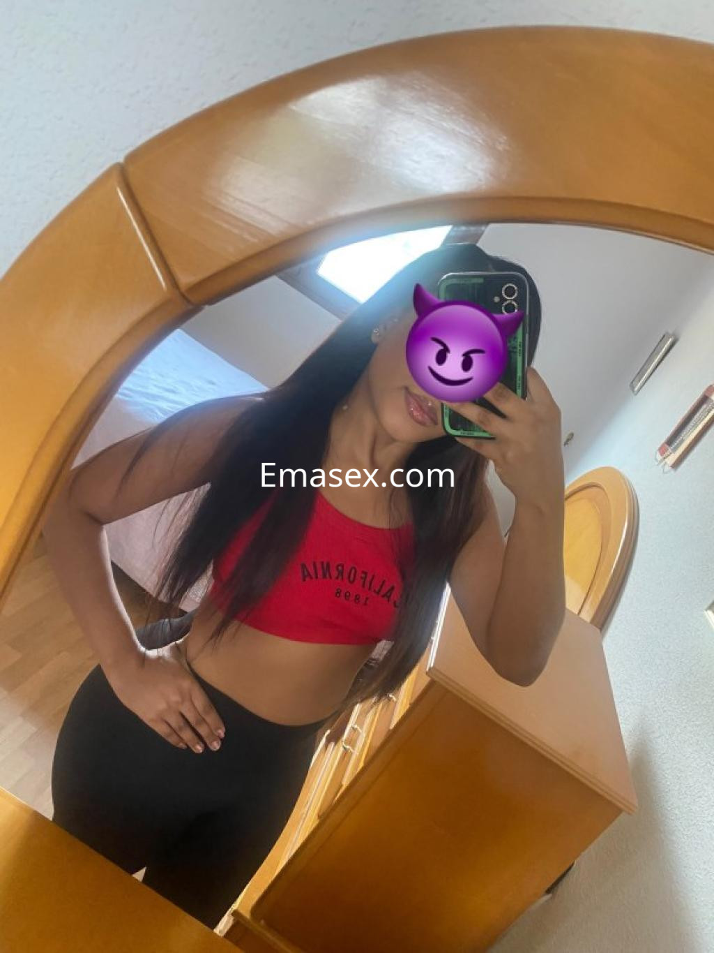 Escort en Castellón, con cabello largo y lacio, viste un top rojo y leggings negros mientras se toma una selfie en un espejo.