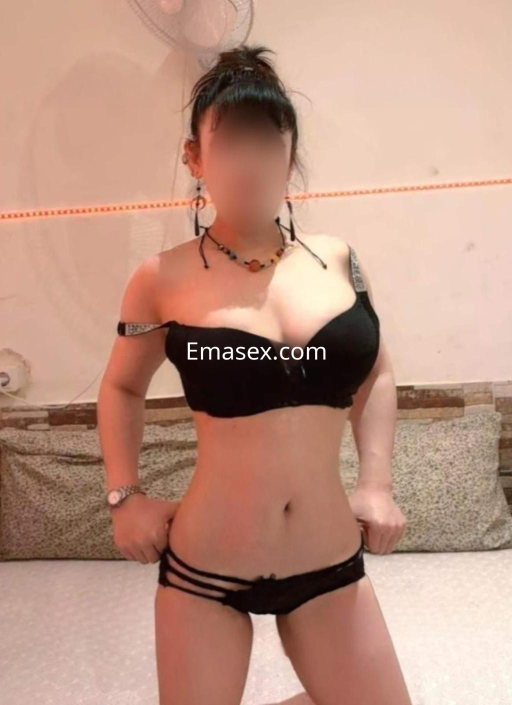 Puta en Barcelona viste un sujetador negro sin mangas y pantalones cortos, posando con un fondo neutro.