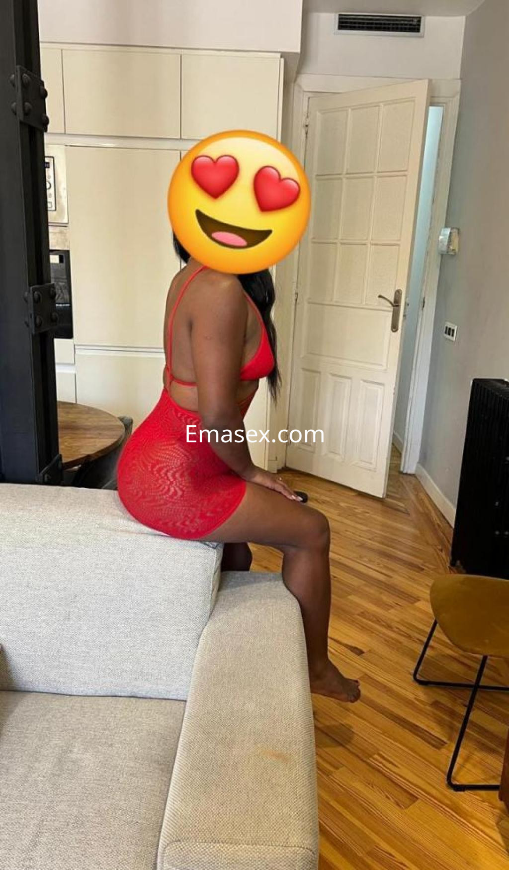 Puta sentada en un sofá, vistiendo un vestido rojo transparente y mostrando una actitud seductora en Madrid.