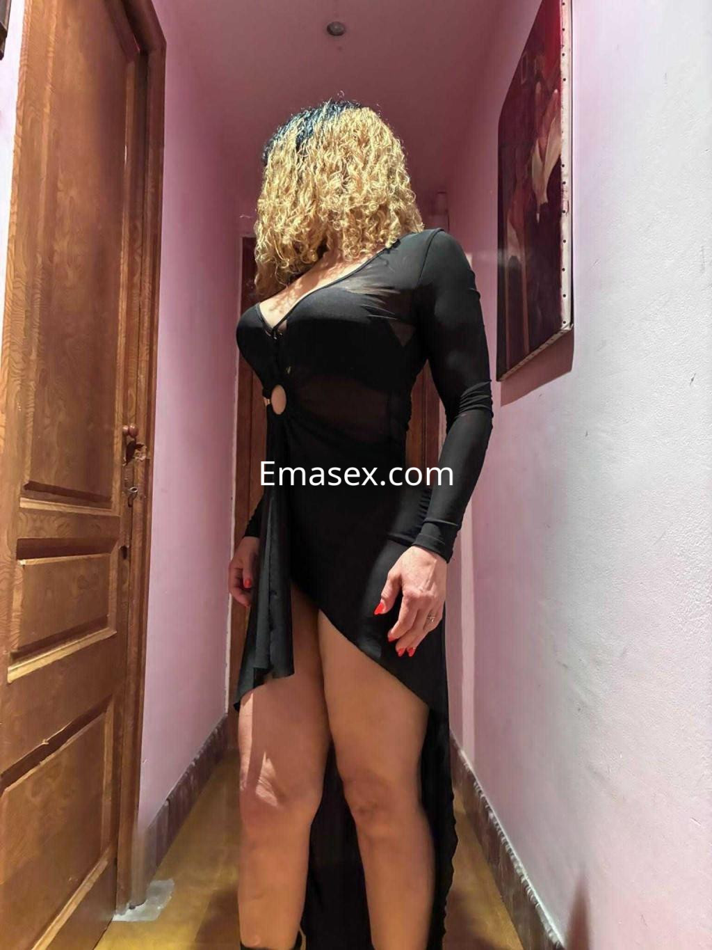 Puta en Barcelona con vestido negro ajustado y transparente, mostrando piernas, en un pasillo iluminado.