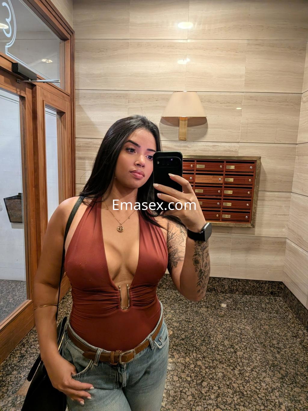 Escort en Pamplona con cabello largo y oscuro, vistiendo un body marrón y jeans, posando frente a un espejo.