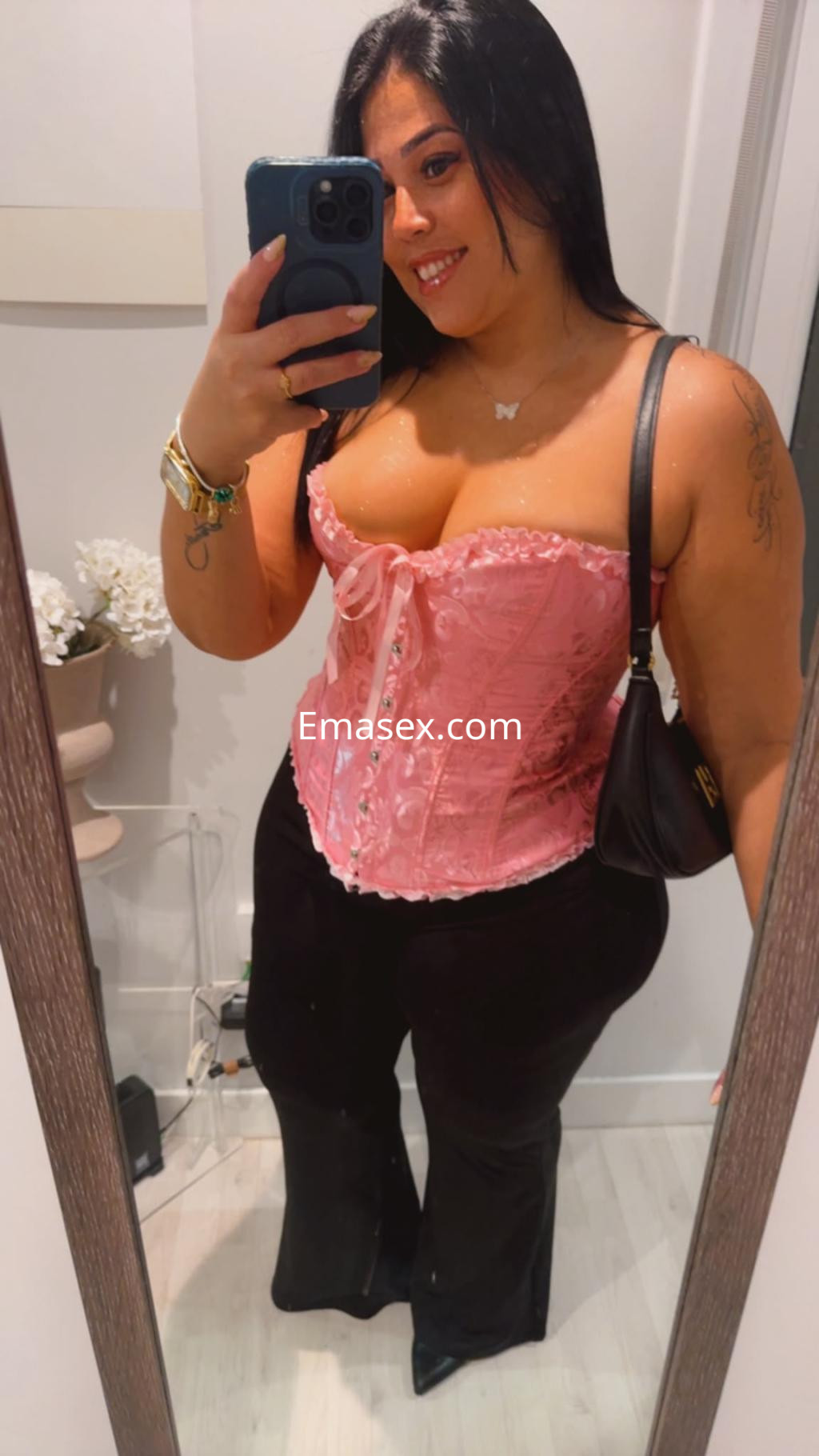 Escort en Donosti luciendo un corset rosa con detalles de encaje y pantalones negros, sonriendo frente al espejo.