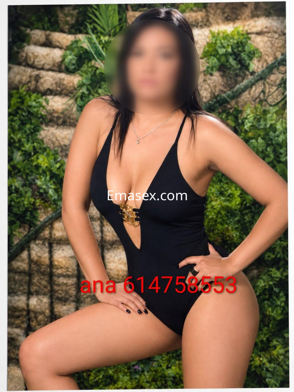 Escort posando en Logroño con traje de baño negro, de escote pronunciado y detalles dorados, en un entorno natural.
