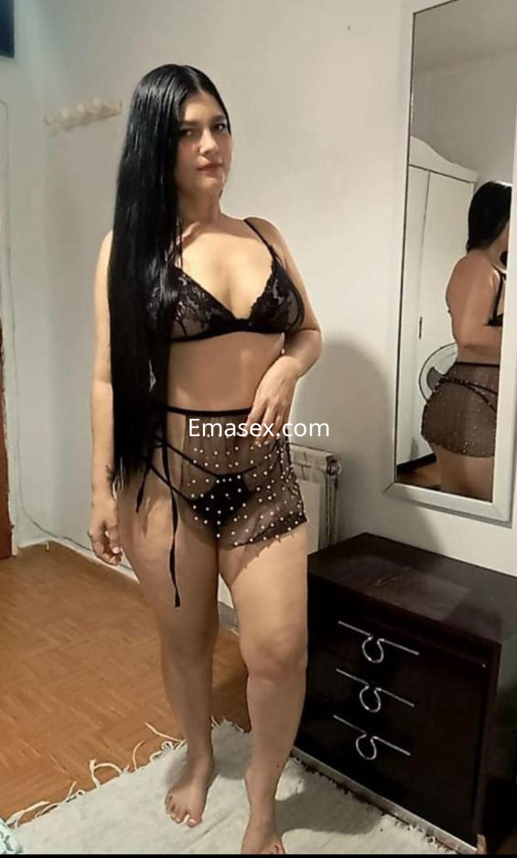 La escort en Cáceres luce una lencería negra con detalles transparentes y una pose elegante frente a un espejo.