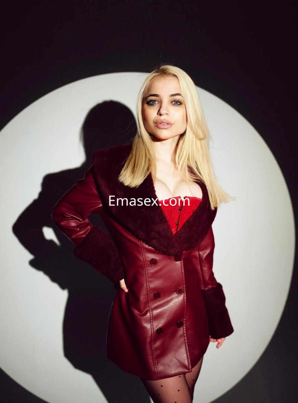 Puta rubia con cabello lacio, viste un abrigo de cuero burdeos y un corset rojo en Barcelona.