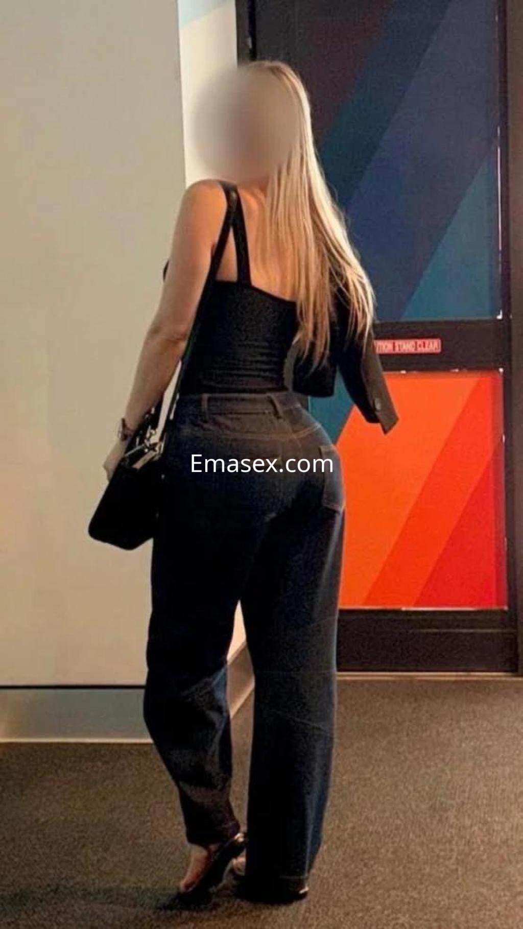 Escort en Las Palmas de espaldas, vistiendo un top negro y pantalones amplios, con cabello largo y lacio.