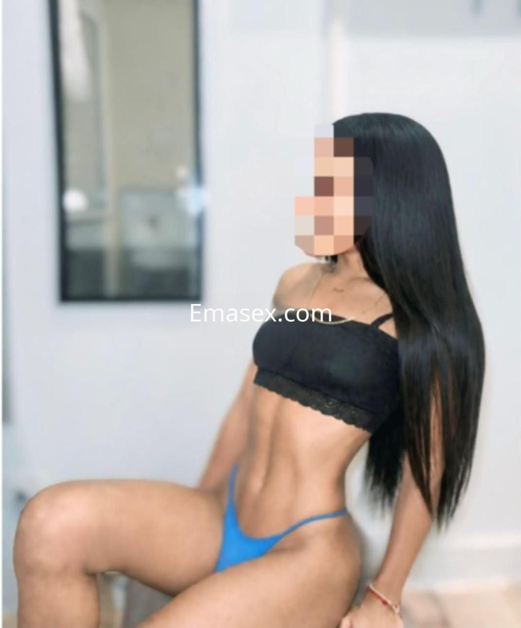 Escort en Badajoz con cabello largo y lacio, vistiendo un top negro y una tanga azul, posando de lado.