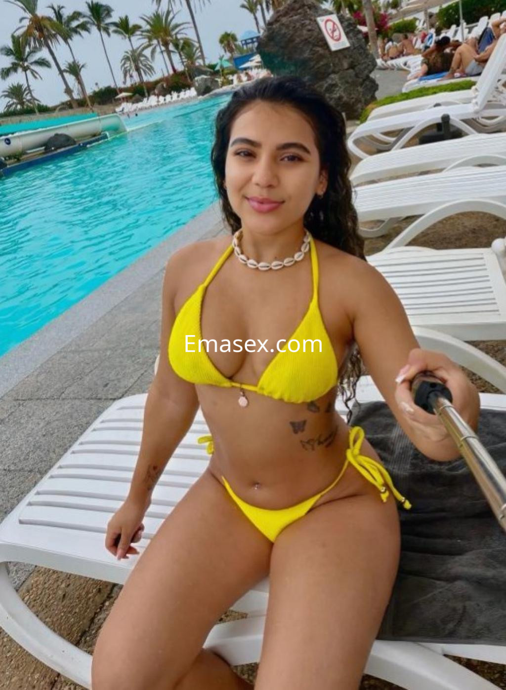 Puta con cabello rizado, usando un bikini amarillo, posa sonriente junto a la piscina en Las Palmas.