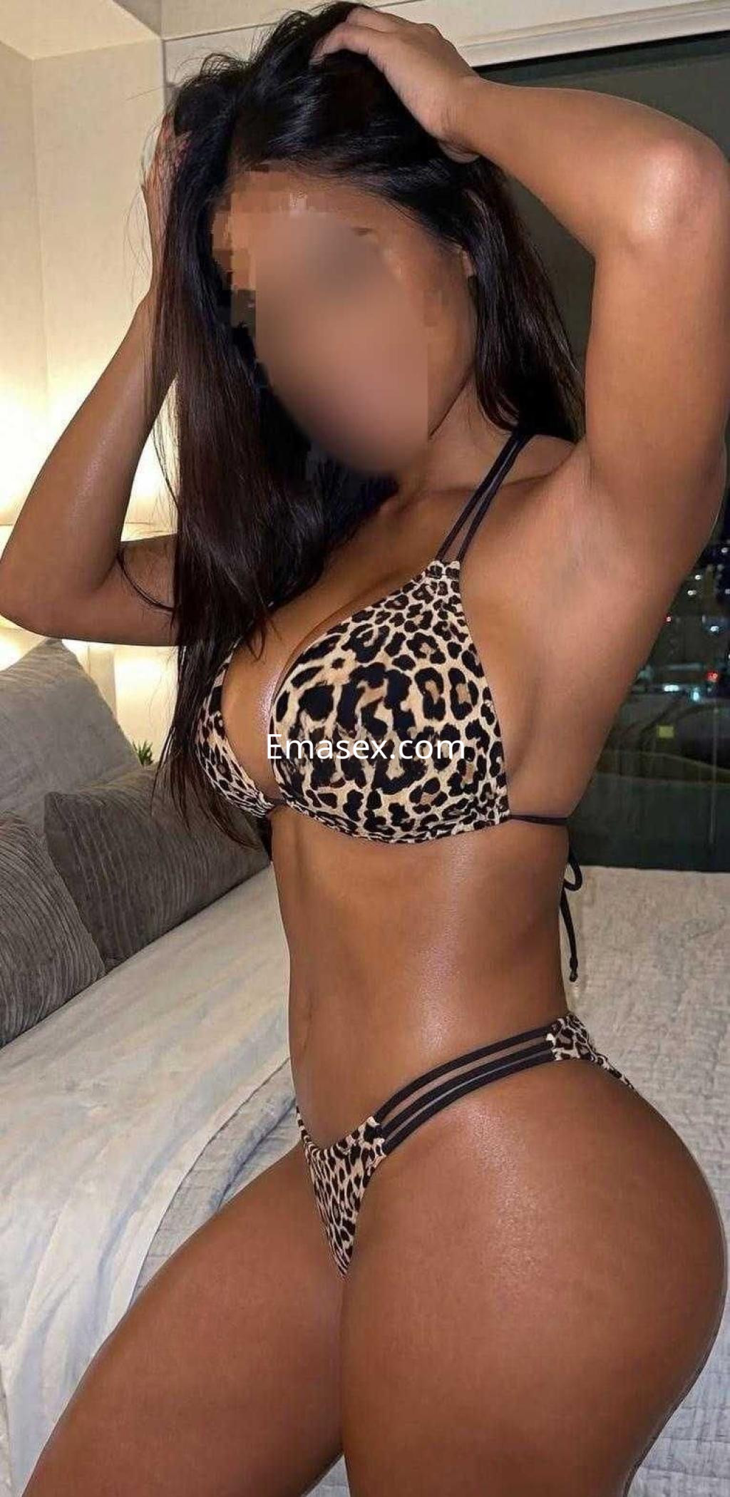 Escort en Córdoba con cabello oscuro, luciendo un bikini de leopardo, posando de lado en un ambiente interior.
