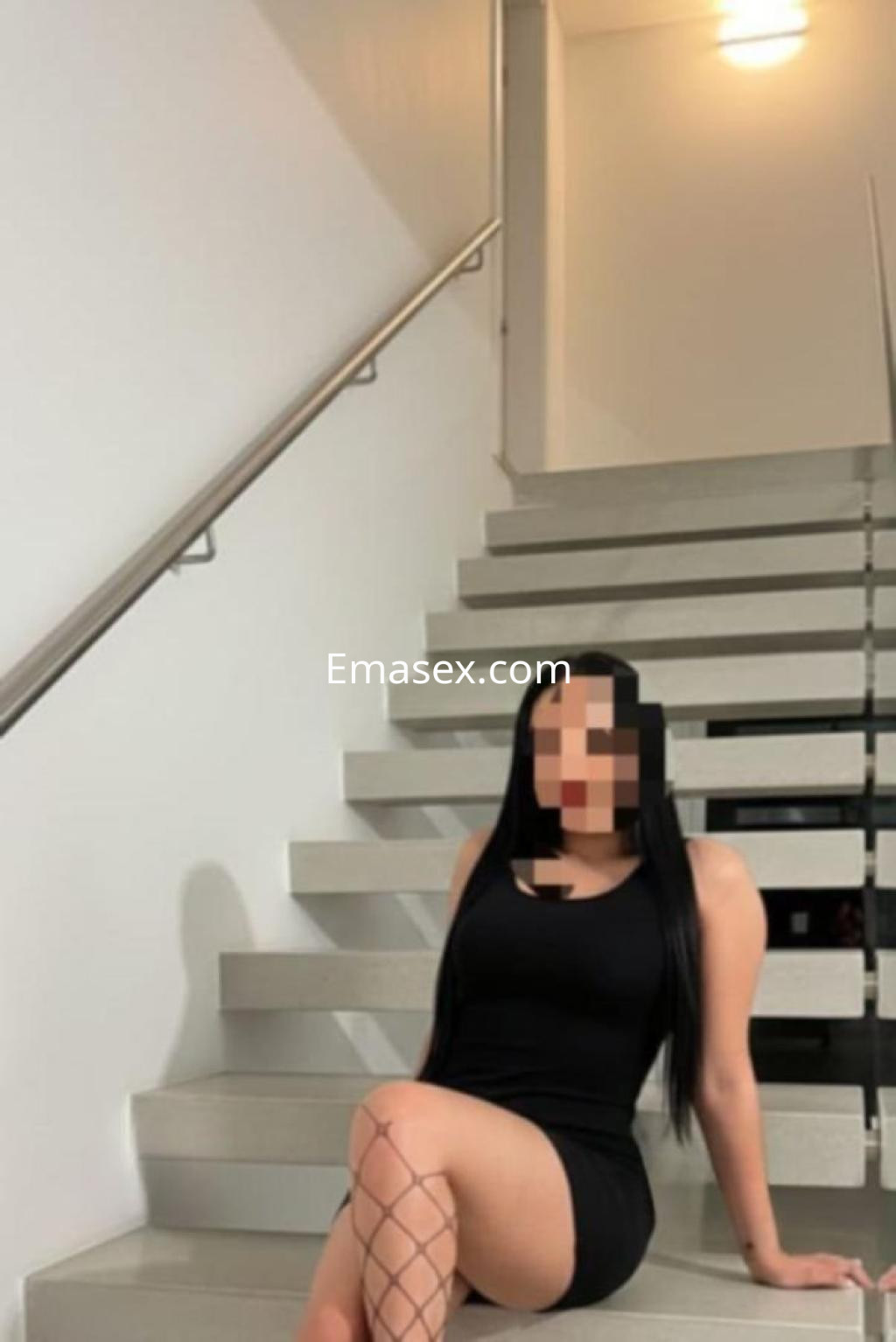 La puta está sentada en unas escaleras, vistiendo un vestido negro y medias de red, en un ambiente moderno de Córdoba.